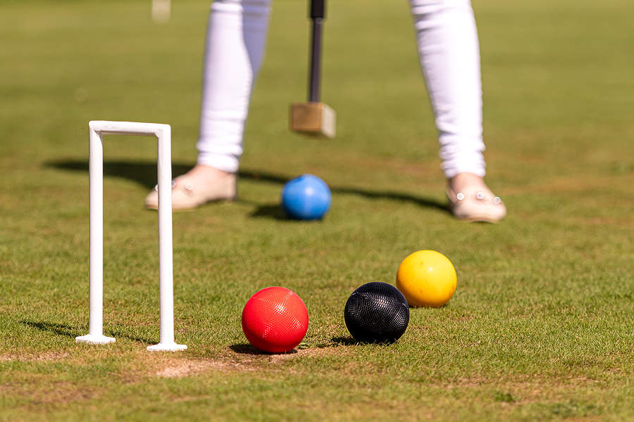 a young woman is playing croquet on a lawn